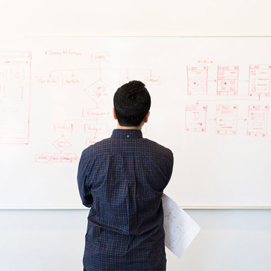 Male student looking a content on whiteboard holding a sheet of paper