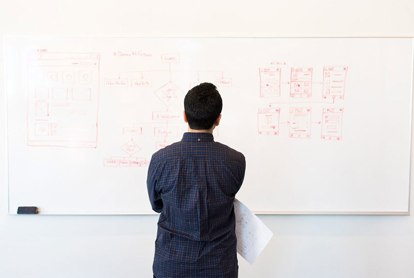 Male student looking a content on whiteboard holding a sheet of paper