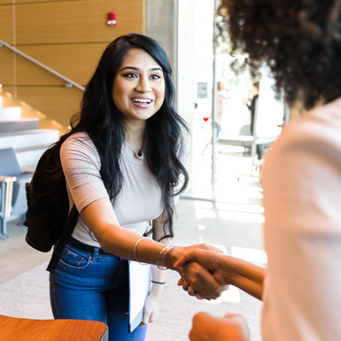 Student smiling and shaking hands with another person in a bright indoor space.