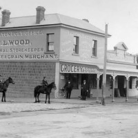 black and white image of old grocery store and people riding horses on the dirt street