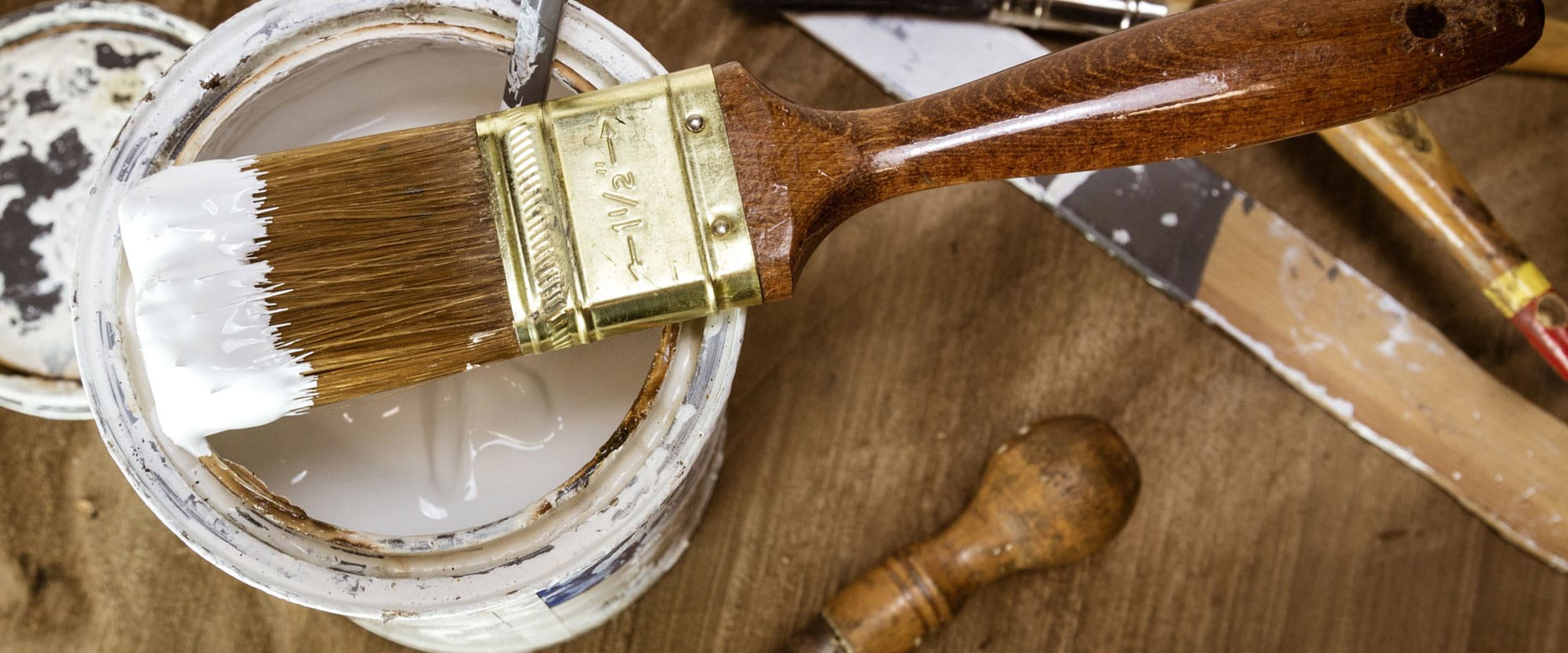 An open paint tin, balancing a paint brush that's on top of the tin