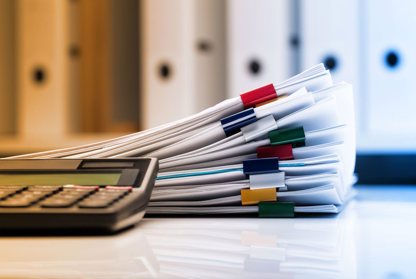 A pile of paperwork sitting on a desk next to a calculator