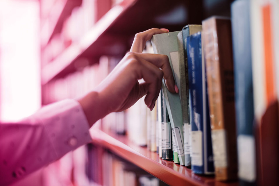 Someone grabbing a book from a library shelf