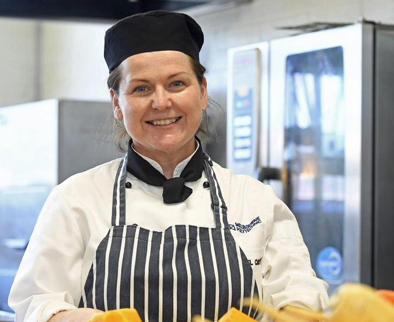 Melbourne polytechnic food staff member smiling at camera while they prepare food.
