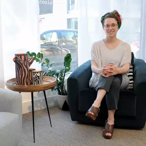 Student sitting at a chair with legs crossed and smiling at camera.