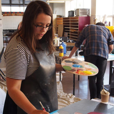 Art student Anna Seed painting on a canvas and with paint palette in other hand