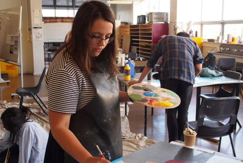 Art student Anna Seed painting on a canvas and with paint palette in other hand