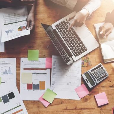 Birds-eye view of charts, sticky notes, calculator, and laptop.