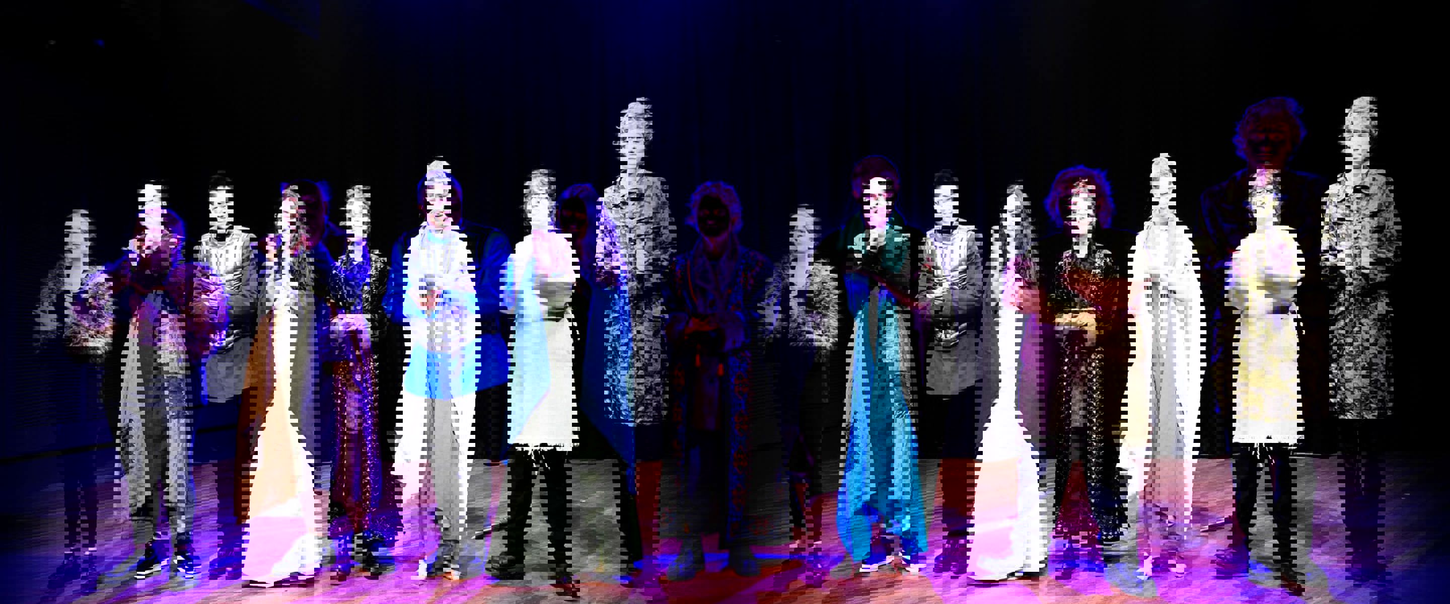 A group of people standing on a stage under theatre lights with costumes on