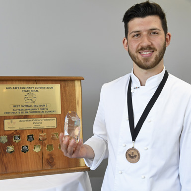 Nickolas Gnafakis standing beside his award and wearing a medal around his neck