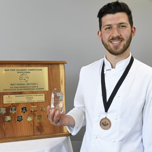 Nickolas Gnafakis standing beside his award and wearing a medal around his neck