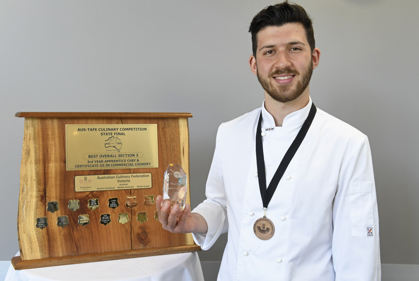 Nickolas Gnafakis standing beside his award and wearing a medal around his neck