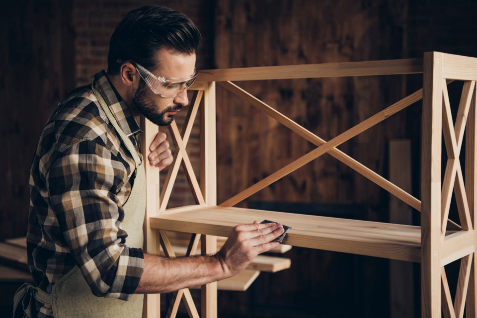 A person sanding down a wooden shelf 