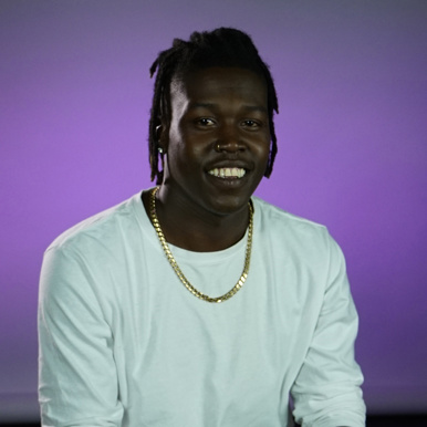 Student sitting and smiling in front of purple background 