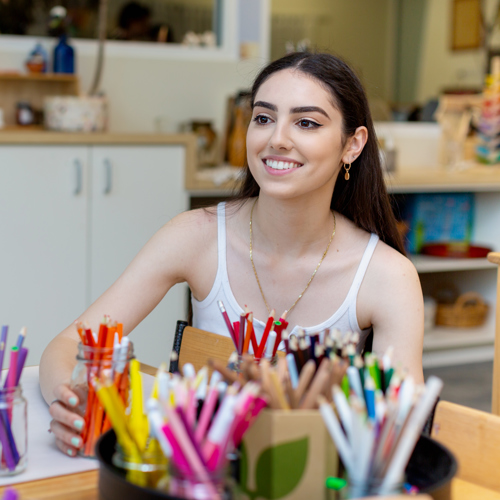 Claudia sitting in front of jars full of coloured pencils