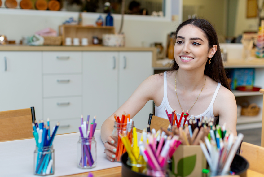 Claudia sitting in front of jars full of coloured pencils