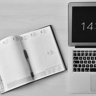 Calendar notebook opened next to a Macbook laptop