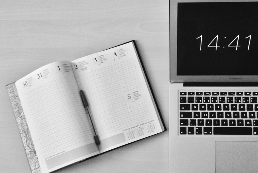 Calendar notebook opened next to a Macbook laptop