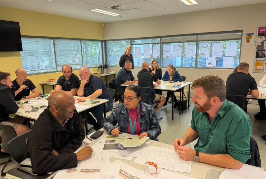 Workshop participants sit at desks with educators and industry representatives.