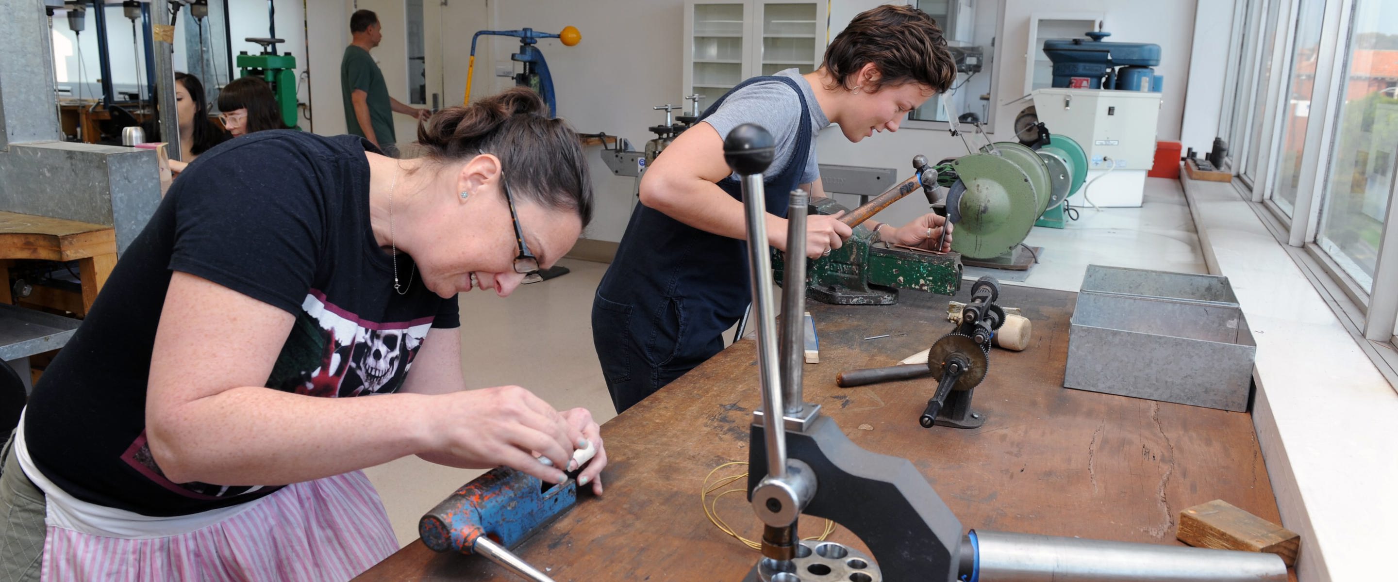 Two jewellery students working with items in vices in the jewellery workshop