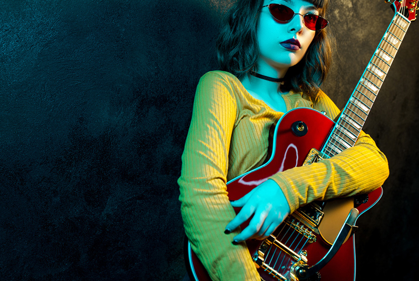 Music student leaning against a dark wall and posing with red electric guitar in arms.