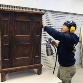 Carpentry student with compressed air lacquer gun and small freestanding cabinet