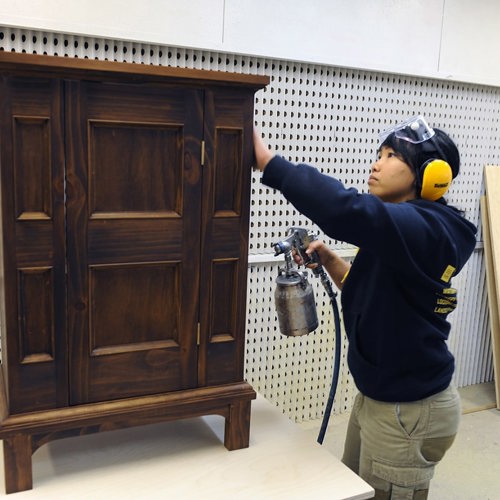 Carpentry student with compressed air lacquer gun and small free standing cabinet