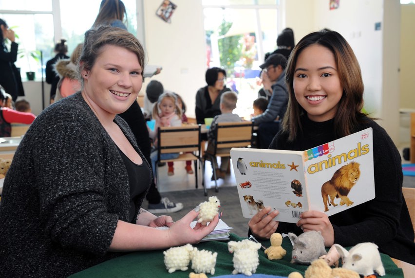 Two young women seated at a table smiling, surrounded by books and toys, engaged in a lively discussion.