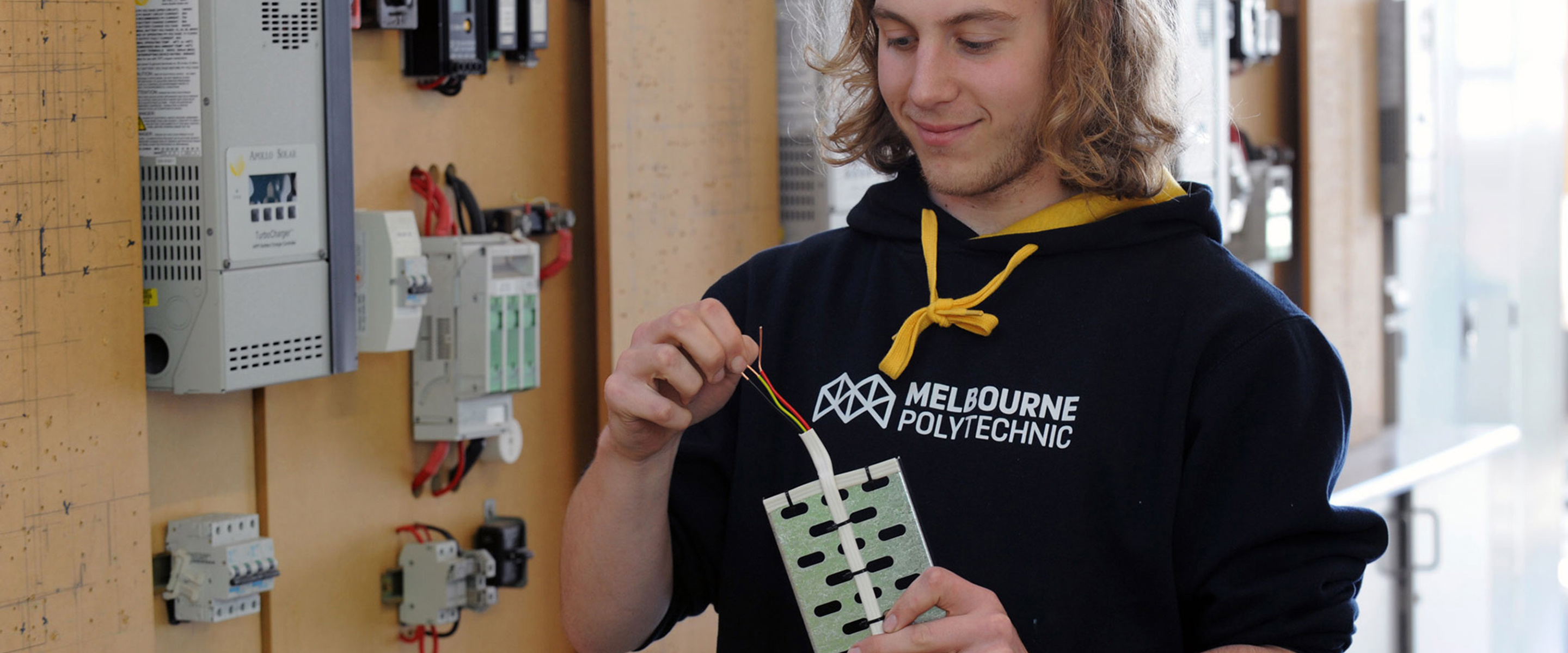 Electronics and Electrical student smiling while holding an electrical cord at a fuse box