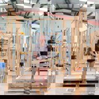 Female carpentry student posing in front of wooden frame work