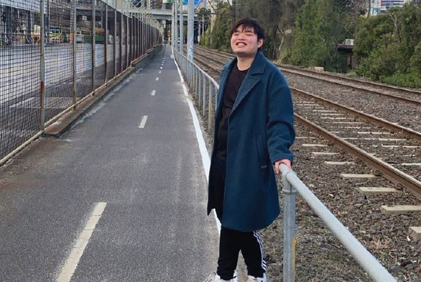 International student Eric Wong in overcoat standing by train rails