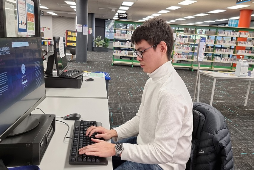 Man wearing a white turtleneck crew while sitting at computer in a Melbourne Polytechnic Library