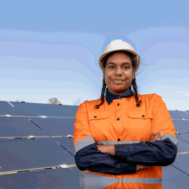 Woman wearing a high-visibility shirt and hard hat, standing in front of a panel structure.