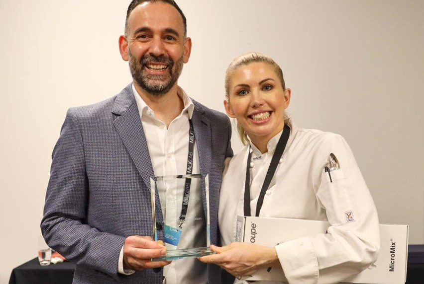 A man and a woman smiling, the woman is being presented with a glass trophy