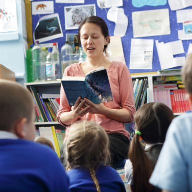 An educator reading to a group of primary school students, seated on the floor.