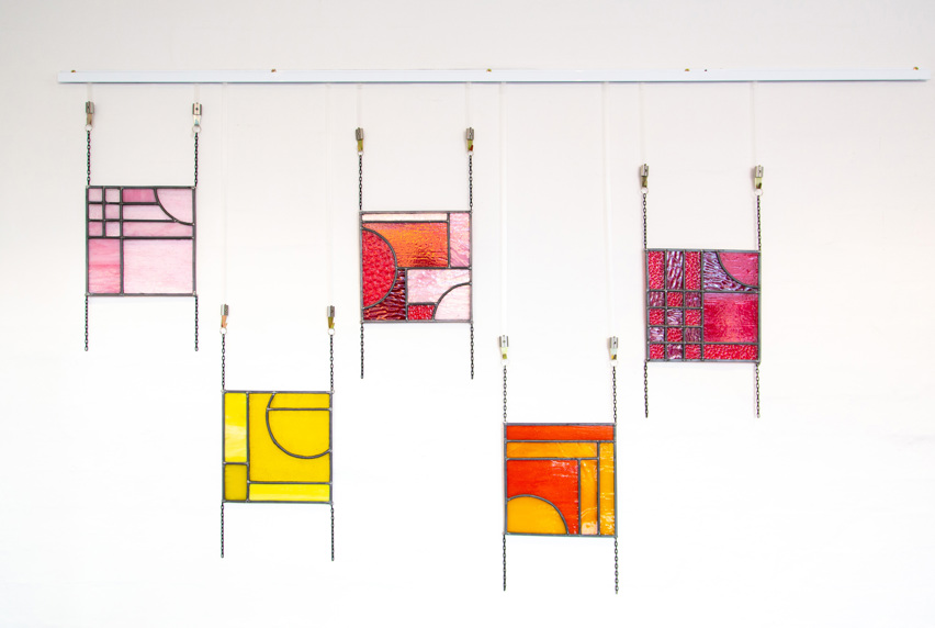 An image of five small coloured stained glass panels hanging on chains against a white background.