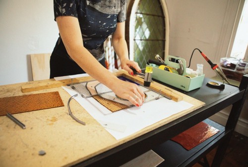 Stained glass artist at work bench applying leadlight to glass.