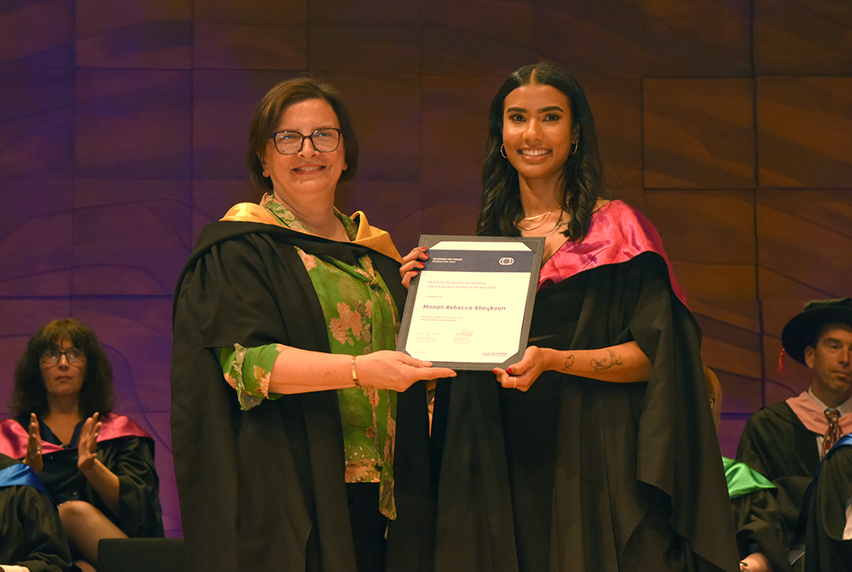 Frances Coppolillo and Rebecca Abeykoon at MP 2024 graduation ceremony dressed in black robes and holding an award.