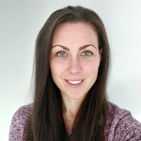 Elisa Gibbs, with long brown hair, wearing a finely knitted pink sweater and smiling.