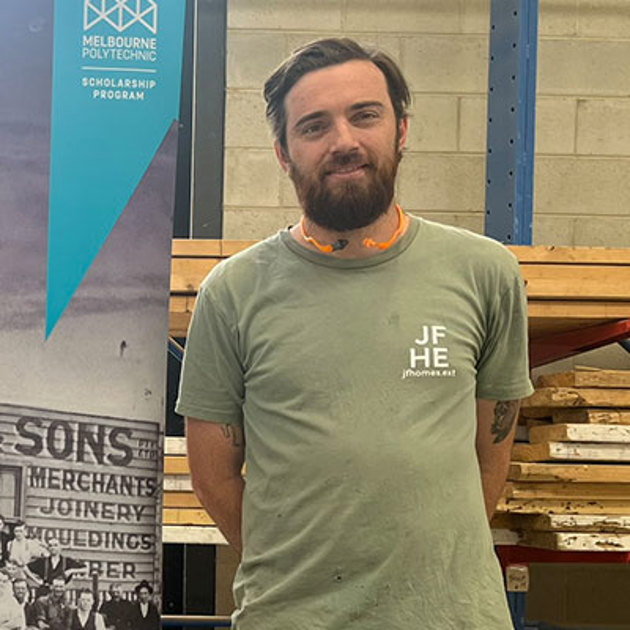 A man smiling stands beside a display banner, with a neutral background and casual attire.
