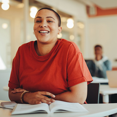 Smiling student at a classroom desk with an open book.