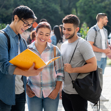 Group of students standing outdoors, looking at a notebook and smiling.