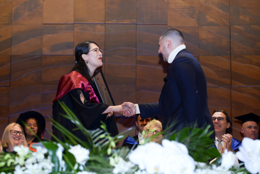 Two people shaking hands on stage wearing formal graduation robes