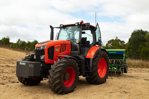 Orange Kubota M7 Tractor parked on short grass with a seed drill and counterweight attached.