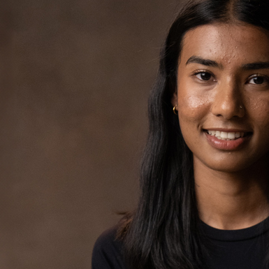 Rebecca Abeykoon, woman with long black hair smiling with a neutral coloured background.