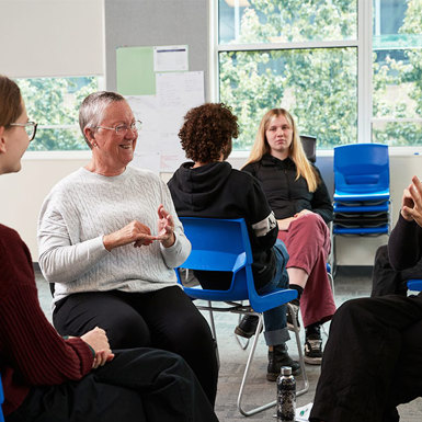 A diverse group of individuals sitting in chairs in a well-lit room, engaged in Auslan. 