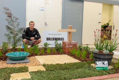 Landscape Construction student next to his landscape project which demonstrates paving, turf, bricklaying, planting, water feature and design.