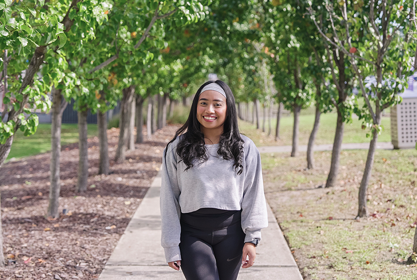 Melbourne Polytechnic alumna smiling at the camera, surrounded by lush green trees on campus.