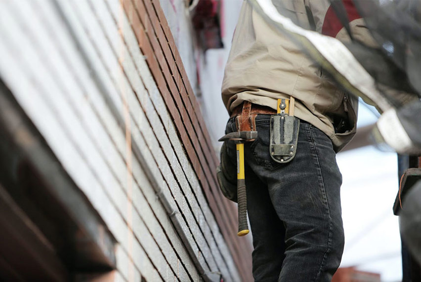 The back of a carpenter showing his tool belt with a hammer and measuring tape