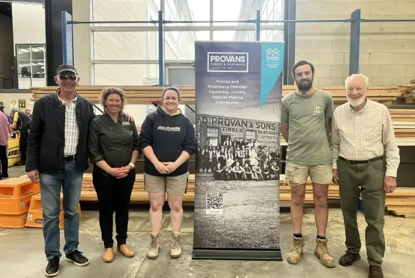 Five people in a construction workshop standing beside a Provan and Rosenberg Families' Scholarship Banner.